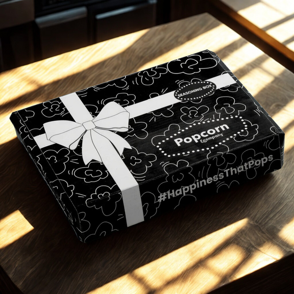 Black box with white ribbon and 'Popcorn' branding on a wooden surface