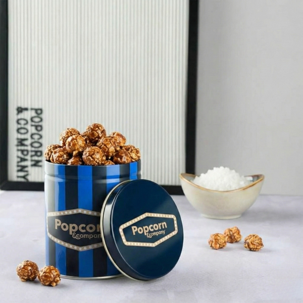Blue and white striped popcorn container with 'Popcorn Company' branding, filled with popcorn, on a light gray surface.